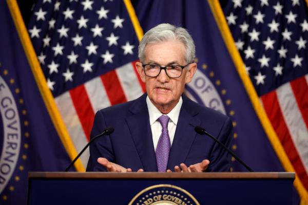 Federal Reserve Bank Chair Jerome Powell announcing unchanged interest rates at a news conference, standing at a podium with microphones