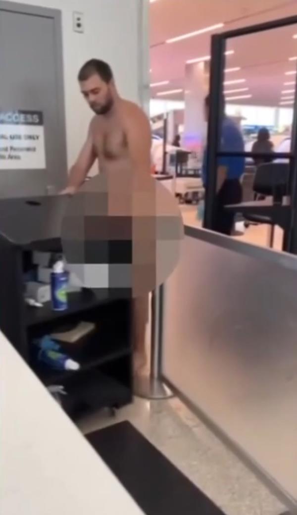 A naked man stands in front of an airport desk, surrounded by TSA agents and sheriff deputies, allegedly drunk and trying to breach security.