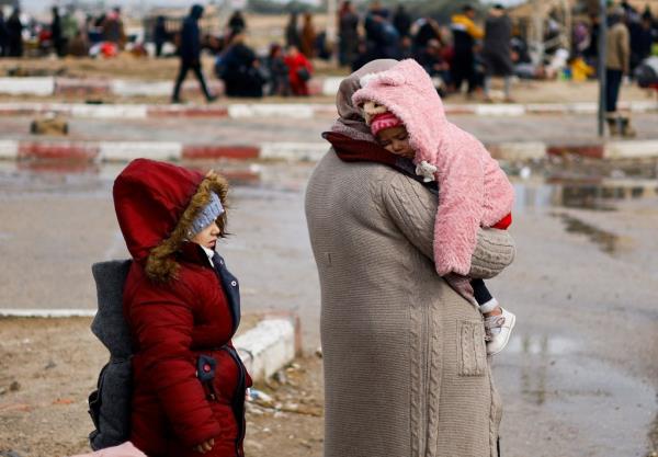 A woman carries a child wearing a pink coat and is followed by an older child in a red coat as Palestinians flee Khan Younis amidst an o<em></em>ngoing co<em></em>nflict in the Gaza Strip.