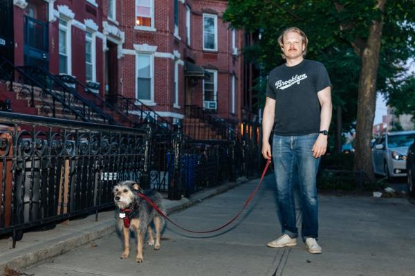 Luna the dog and Zach Henson stand on a Crown Heights sidewalk at dusk. 