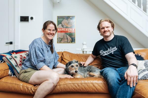 Stephanie Henson and Zachary Henson sit on a leather couch, their dog Luna lying between them. 
