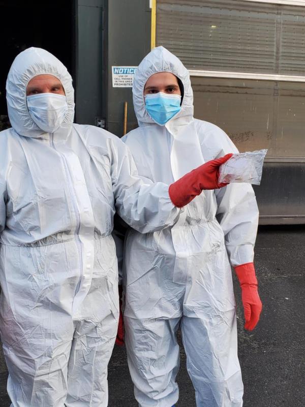 Two people wearing head-to-toe white suits with masks and gloves. One hold a sandwich bag co<em></em>ntaining jewelry.