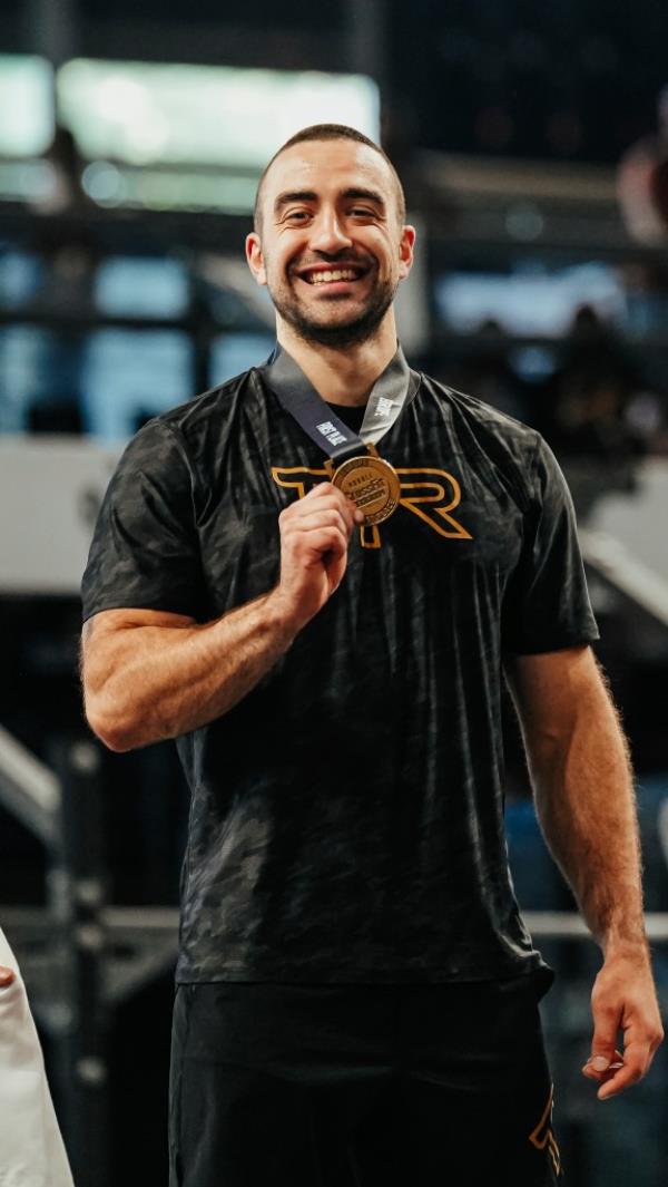 Dukic smiles while holding a medal he is wearing around his neck