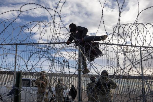 A migrant climbs over Texas' border fence