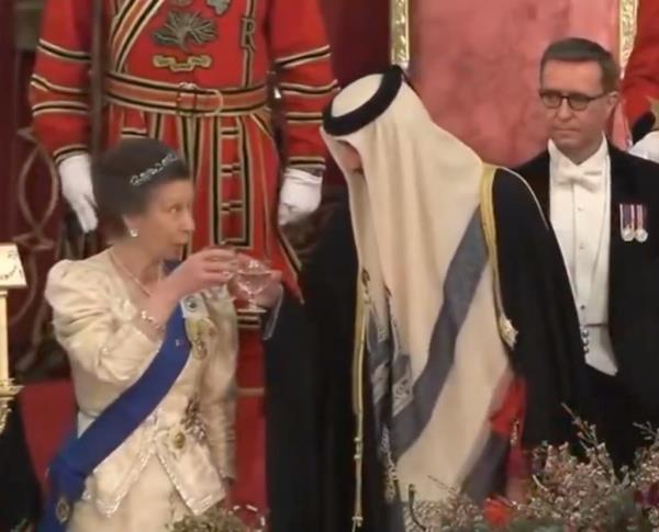 Princess Anne in a white dress seated next to Sheikh Tamim bin Hamad Al Thani in a white robe, sharing an awkward moment at a Buckingham Palace state banquet