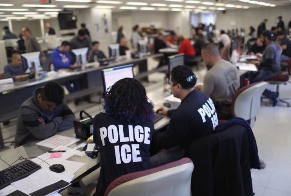 Two workers in T-Shirts that read POICE ICE sit at their desks in a busy office 