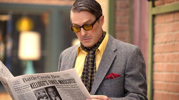 Hugh Grant as Thurl Ravenscroft reading a newspaper in Unfrosted The Pop-Tart Story